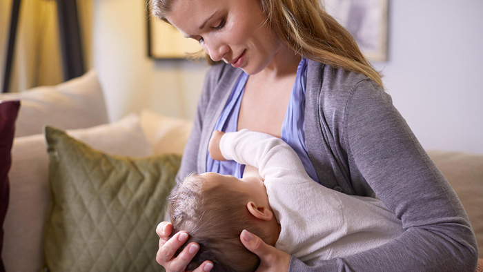 A mother breastfeeds a baby in the football hold position.
